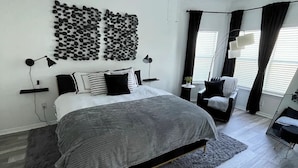 A modern bedroom with a large bed, a ceiling fan, a wall-mounted light, and a decorative wall piece.