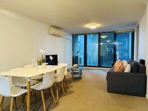 A modern living room with a dining area, a sofa, and a large window with a view. - Spacious City Road Haven (Southbank)