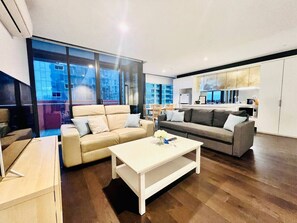 A modern living room with a sofa, a coffee table, and a kitchen area visible through a glass partition. - Chic Urban Getaway–Two 3BR Apartments in Rose Lane (Melbourne)