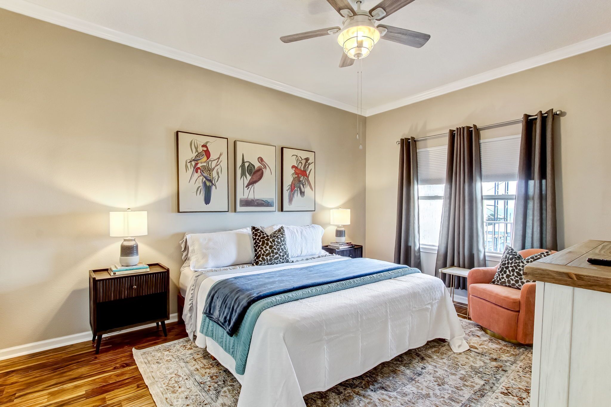 A bedroom with a bed, nightstands, a desk, a chair, a ceiling fan, and artwork on the wall.