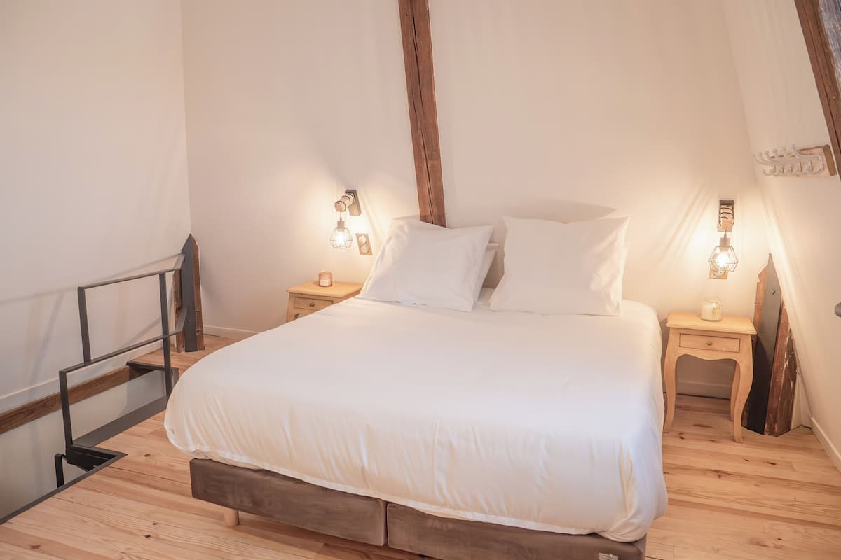 A bedroom with a large bed, wooden headboard, two bedside tables with lamps, and a wooden floor.