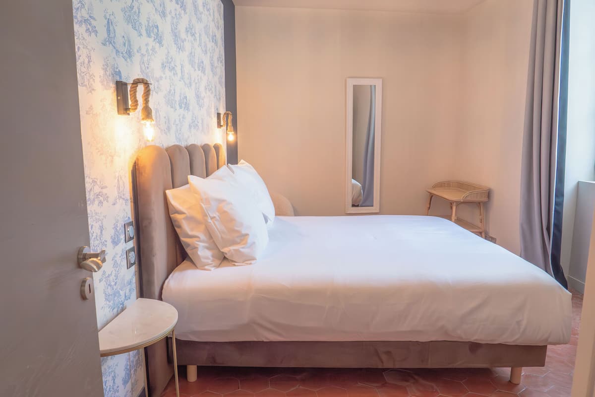 A neatly made bed with white linens and a headboard with wall-mounted lights.