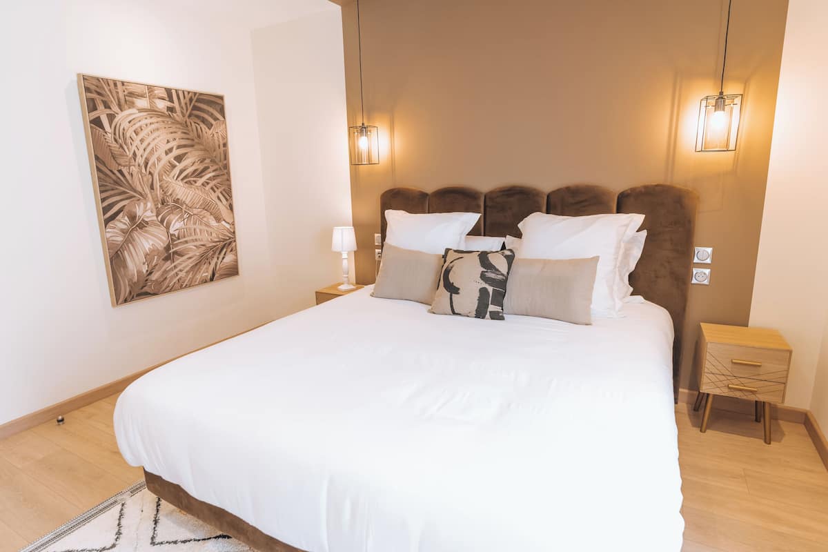 A neatly made bed with white linens, a headboard with a brown upholstered panel, and a wall-mounted light fixture.