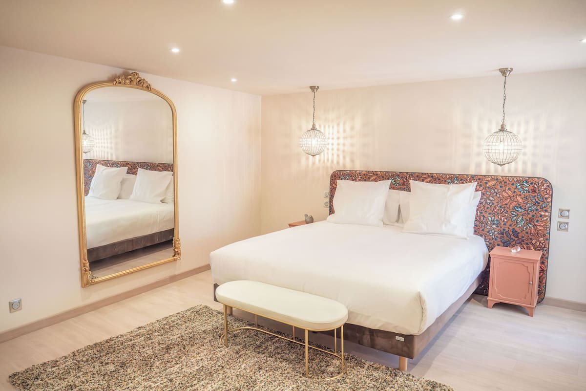 A bedroom with a large bed, a bench, a nightstand, a mirror, and two wall-mounted lights.