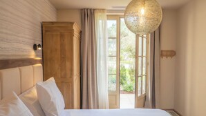 A bedroom with a bed, a wooden wardrobe, a large window with curtains, and a hanging light fixture.
