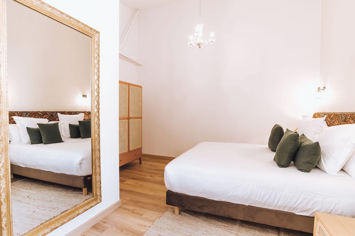 A bedroom with two beds, a large mirror, a chandelier, and a wooden wardrobe.