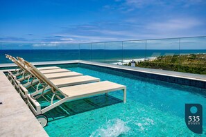 Un área de piscina con sillones de descanso y vista al océano.