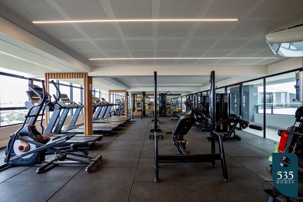 A modern gym with treadmills, weight machines, and a large window providing natural light.