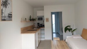 Una cocina moderna con encimera de madera, un fregadero y un microondas. Hay una pequeña mesa de comedor y una cama con manta blanca.