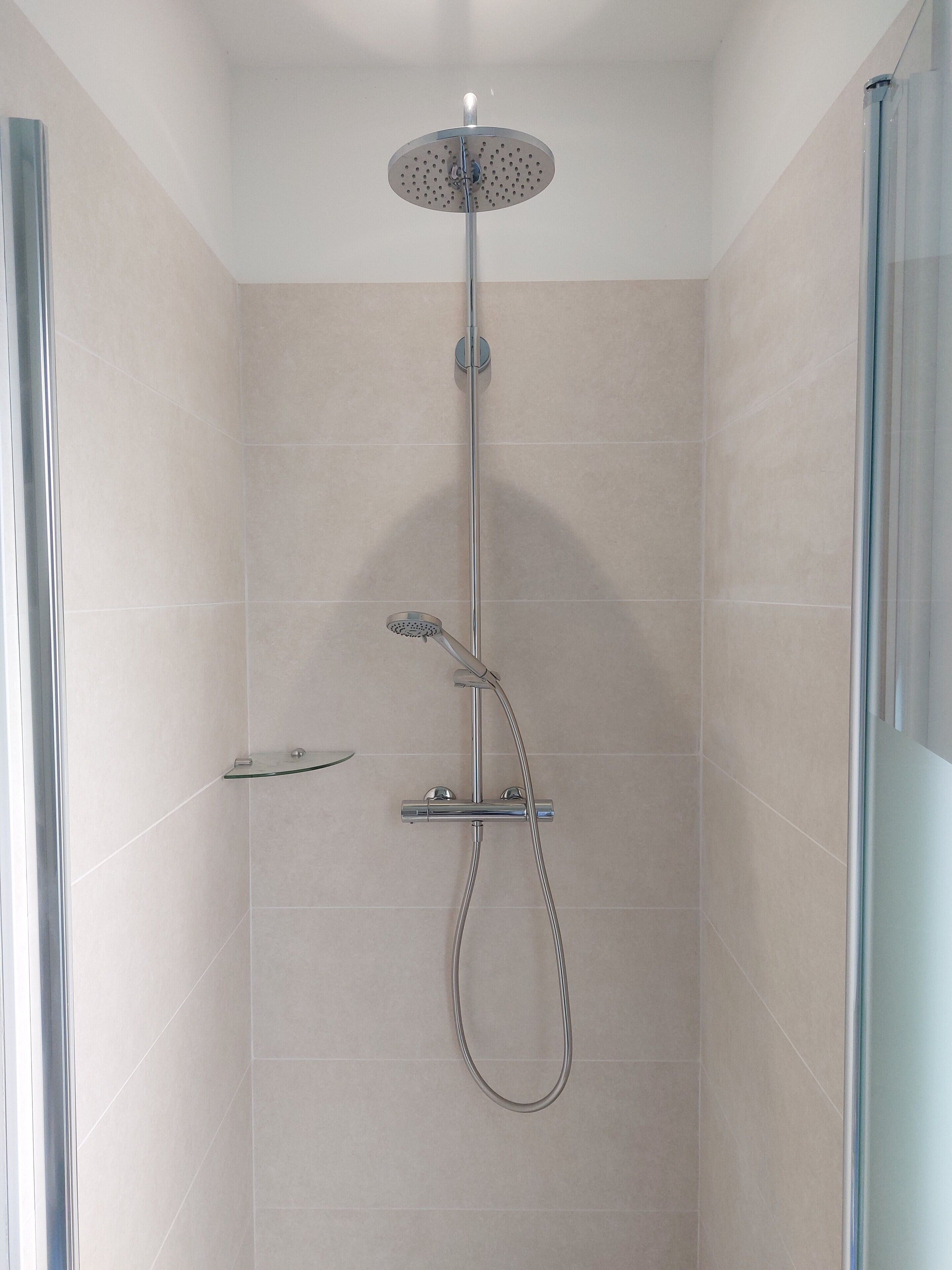 Een moderne douche met een handdouche, regendouche en een douchehouder.