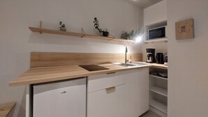 Una cocina moderna con encimera de madera, lavavajillas integrado, un fregadero y un microondas. Hay estantes con plantas y una cafetera.