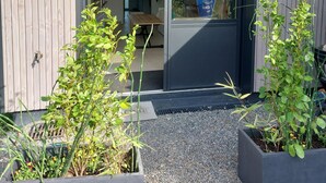 Entrada de un edificio moderno con fachada de madera, puerta de cristal y un pequeño jardín con plantas en macetas.