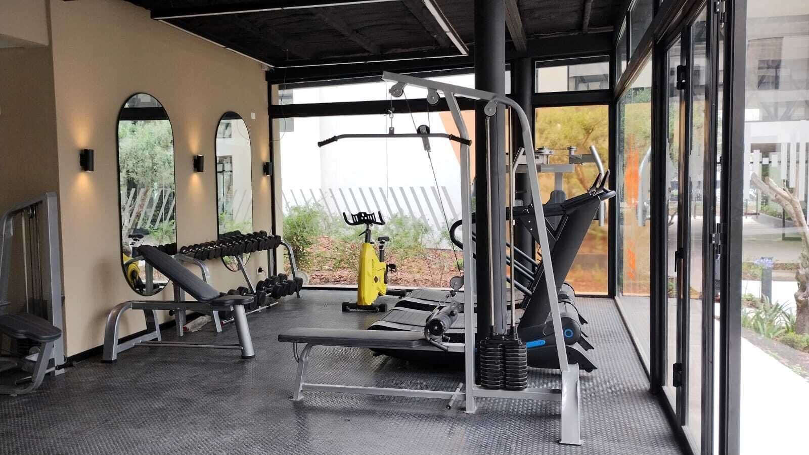 Et fitnessrum med træningsudstyr, spejle og udsigt til det fri.