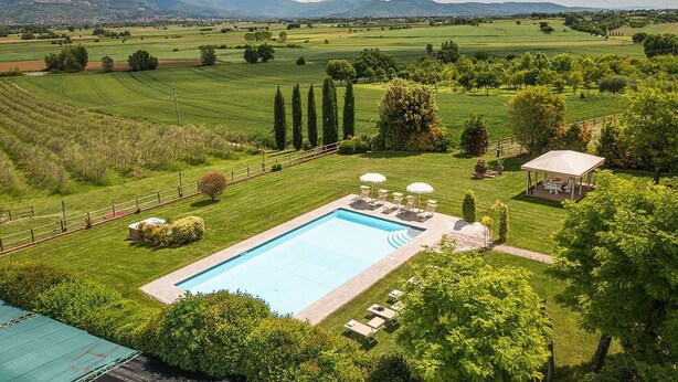 Une piscine entourée d’une pelouse parfaitement entretenue, avec un belvédère et des chaises longues à proximité.