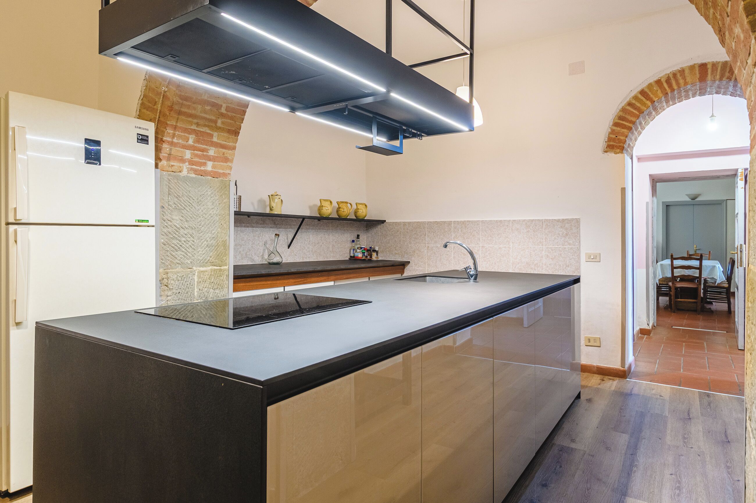 A modern kitchen with a central island, a built-in oven, and a brick accent wall.