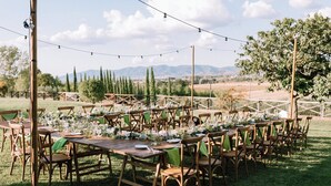 Un espace de restauration en plein air avec des tables et des chaises en bois, des guirlandes lumineuses et une vue sur la campagne.