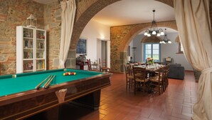 Une table de billard, un coin repas avec des chaises et un mur en pierre.