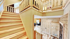 Una escalera de madera que lleva a un altillo con una mesa y sillas a la vista en el fondo.