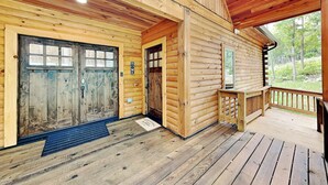 Una cabaña de madera con un porche, una entrada de doble puerta y un ventanal pequeño.