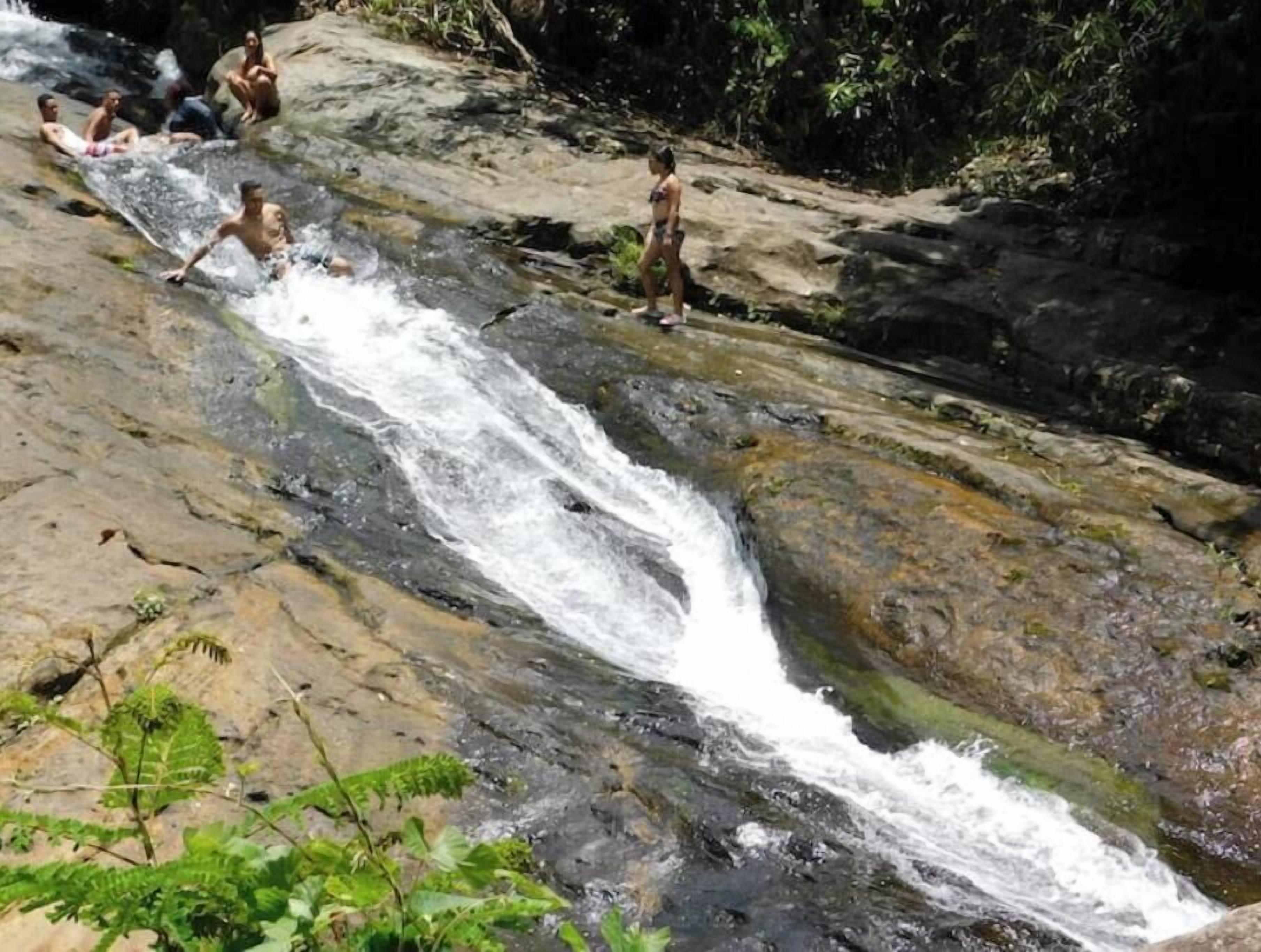 Una cascada con gente sentada y de pie sobre rocas.