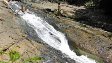 Una cascada con gente sentada y de pie sobre rocas.