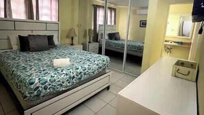 A bedroom with a bed, a bedside table, a mirror, and a sliding door leading to another room.