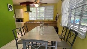 A dining area with a long table and chairs, a ceiling fan, and a window with blinds.