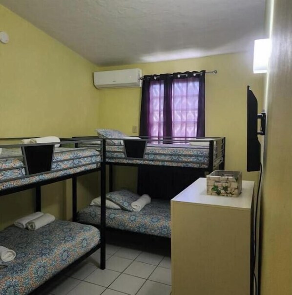 A dormitory room with bunk beds, a small desk, a window with curtains, and an air conditioning unit. - Villa del Rio in Hacienda Monte Rey
(Luquillo)