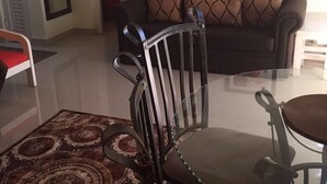 Un salon avec un canapé de couleur foncée, un tapis à motifs, une table en verre et une chaise à armature métallique.