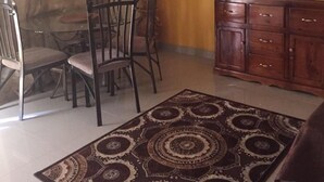 Un coin repas avec une table et des chaises, un téléviseur posé sur un meuble en bois et un tapis à motifs sur le sol.