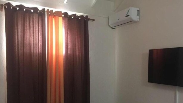 Une chambre comprenant un lit, un téléviseur fixé au mur, une petite étagère avec quelques objets et un appareil de climatisation.
