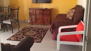 Un salon avec un canapé, un fauteuil rouge, un meuble en bois, une télévision et un ventilateur de plafond.
