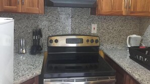 Une cuisine dotée de plans de travail en granit, d’une cuisinière noire, d’armoires en bois et d’une hotte intégrée.