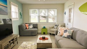 A living room with a flat-screen TV, two sofas, a coffee table, and a window with blinds. - Surfside Beach Bungalow- spectacular views of Rudee Inlet! (Virginia Beach)