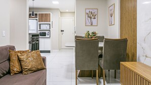 Ein modernes Wohnzimmer mit einer Couch, einem Esstisch und Stühlen. Im Hintergrund ist eine Küche mit sichtbaren Geräten erkennbar.