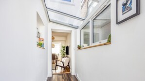 Ein schmaler Flur mit Holzboden, einem Oberlicht, einem Essbereich im Hintergrund und einem gerahmten Bild an der Wand.