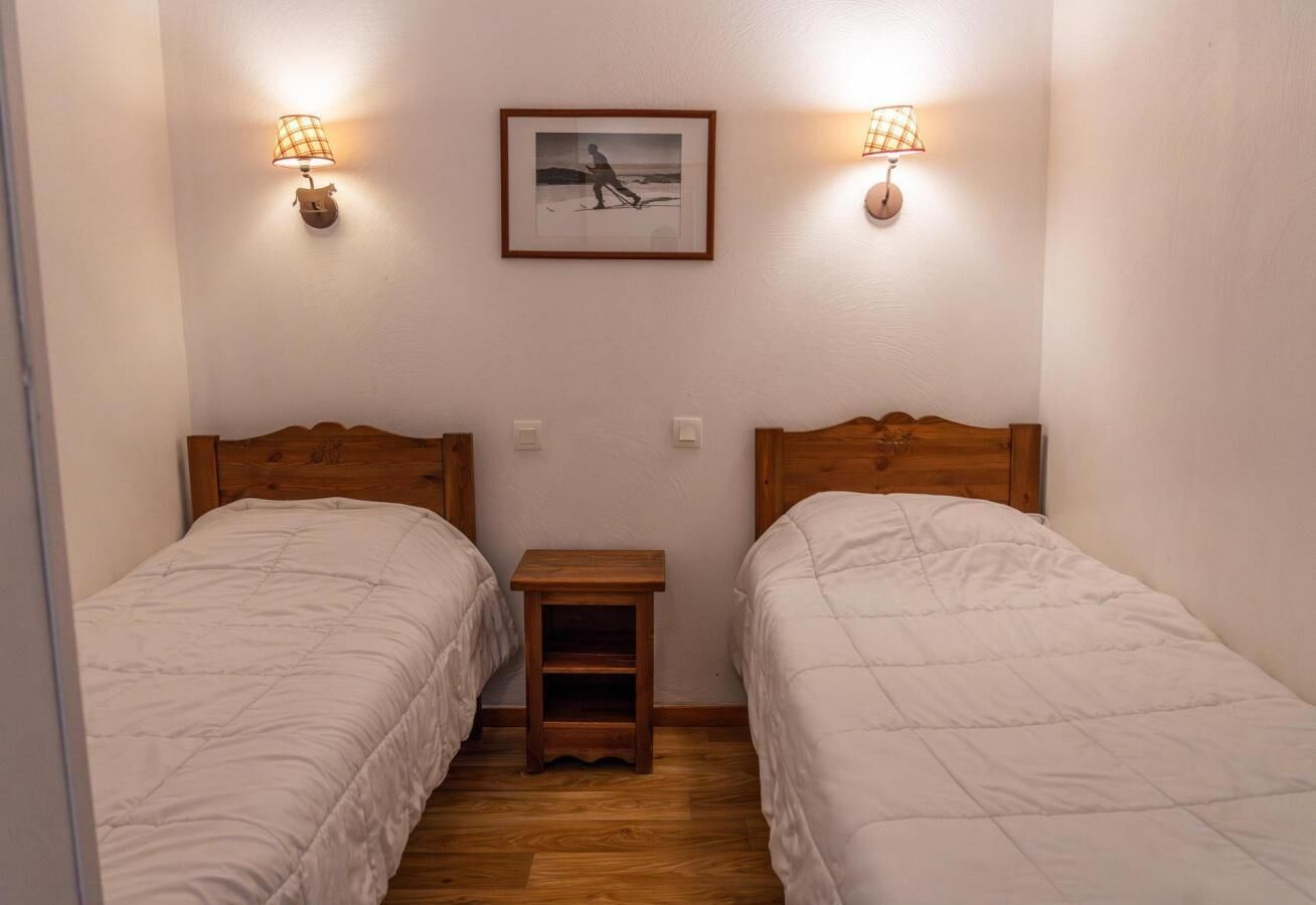 A small, cozy room with two single beds, a small wooden nightstand, and two wall-mounted lamps.