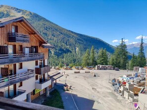 A multi-story wooden building with balconies, a parking area with vehicles, and a mountainous backdrop.