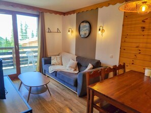A cozy living area with a sofa, a small round table, and a wooden dining table. - 40m from ski slopes, 2nd floor, fitness, swimming pool, sauna, balcony, tv, ski locker, 35m² (Les Orres)