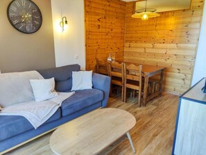 A cozy room with a blue sofa, a wooden dining table, a wall clock, and a hanging light fixture.