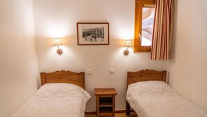 A small, cozy room with two wooden beds, a nightstand, and a framed picture on the wall. - 40m from ski slopes, 1st floor, view mountain, fitness, swimming pool, sauna, balcony, tv (Les Orres)