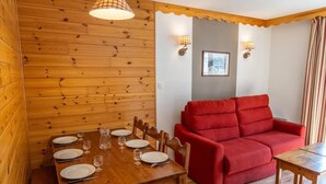 A wooden-paneled room with a dining table set for four, a red sofa, and two wall-mounted lamps. - 40m from ski slopes, 1st floor, view mountain, fitness, swimming pool, sauna, balcony, tv (Les Orres)
