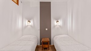A small, clean room with two single beds, a wooden nightstand, and wall-mounted lights.