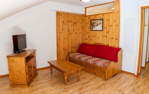 A cozy room with a wooden sofa, a TV on a wooden cabinet, and a small wooden table.