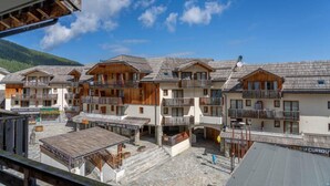 Eine Reihe von Chalets mit Balkonen, einem Steinhof und einer Bergkulisse.