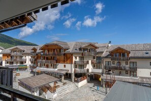A row of chalet-style buildings with balconies, a stone courtyard, and a mountainous backdrop.