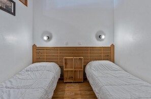 A small, simple room with two single beds, wooden headboard, and two wall-mounted lights.