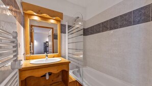 A bathroom with a wooden vanity, a white sink, a mirror, a shower, and a bathtub.
