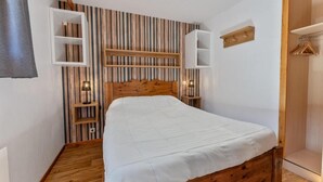 A bedroom with a wooden bed, a sloped ceiling, and built-in wooden shelving. - 40m from ski slopes, 2nd floor, view mountain, fitness, swimming pool, sauna, balcony, tv (Les Orres)