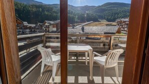 A balcony with two white plastic chairs and a table, overlooking a mountainous landscape with buildings and a railway track. - 40m from ski slopes, 2nd floor, view mountain, fitness, swimming pool, sauna, balcony, tv (Les Orres)